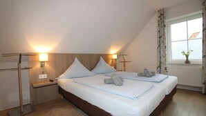 A bedroom with a large bed, two bedside tables, wall-mounted lamps, a window with curtains, and a radiator. - ROB 17 for 6 persons, approx. 86 sqm, pets - Feriendorf Robbenplatte Burhave (Butjadingen)