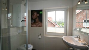 Un bagno moderno con box doccia in vetro, lavabo bianco e finestra vista su un edificio in mattoni.