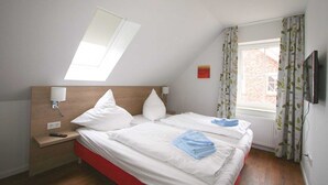 Una camera d'albergo con due letti, un lucernario, una finestra con tende, una TV e un comodino con una lampada.