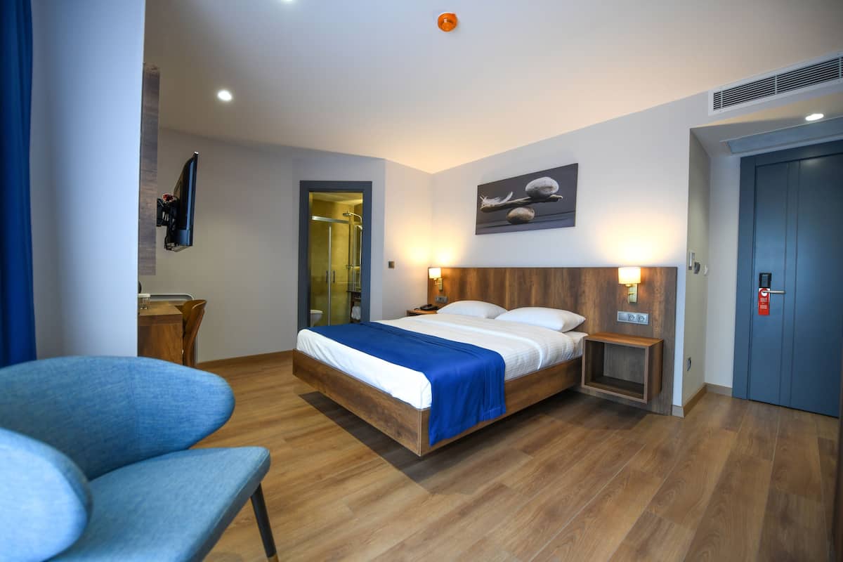 Ein modernes Hotelzimmer mit einem Holzbett, einem Schreibtisch, einem Stuhl und einer Dusche.
