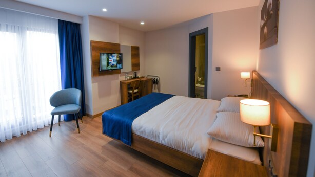 A hotel room with a bed, a desk, a chair, a television, and a bathroom door. - Ref Inn Hotel (Ordu)