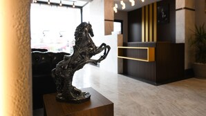 A reception desk with a modern design, a bronze horse sculpture on a wooden pedestal, and a potted plant to the right. - Ref Inn Hotel (Ordu)