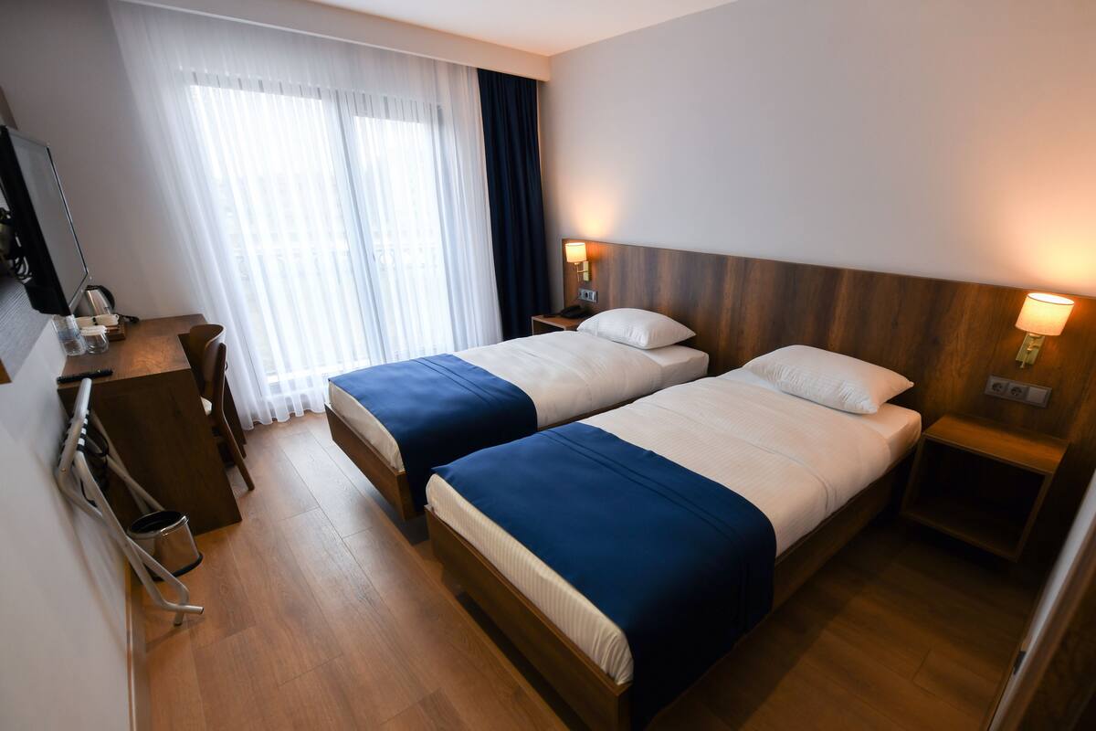 Ein Hotelzimmer mit zwei Betten, einem Schreibtisch, einem Stuhl, einem Fernseher und einem Fenster mit Vorhängen.