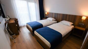 A hotel room with two beds, a desk, a chair, a TV, and a window with curtains.