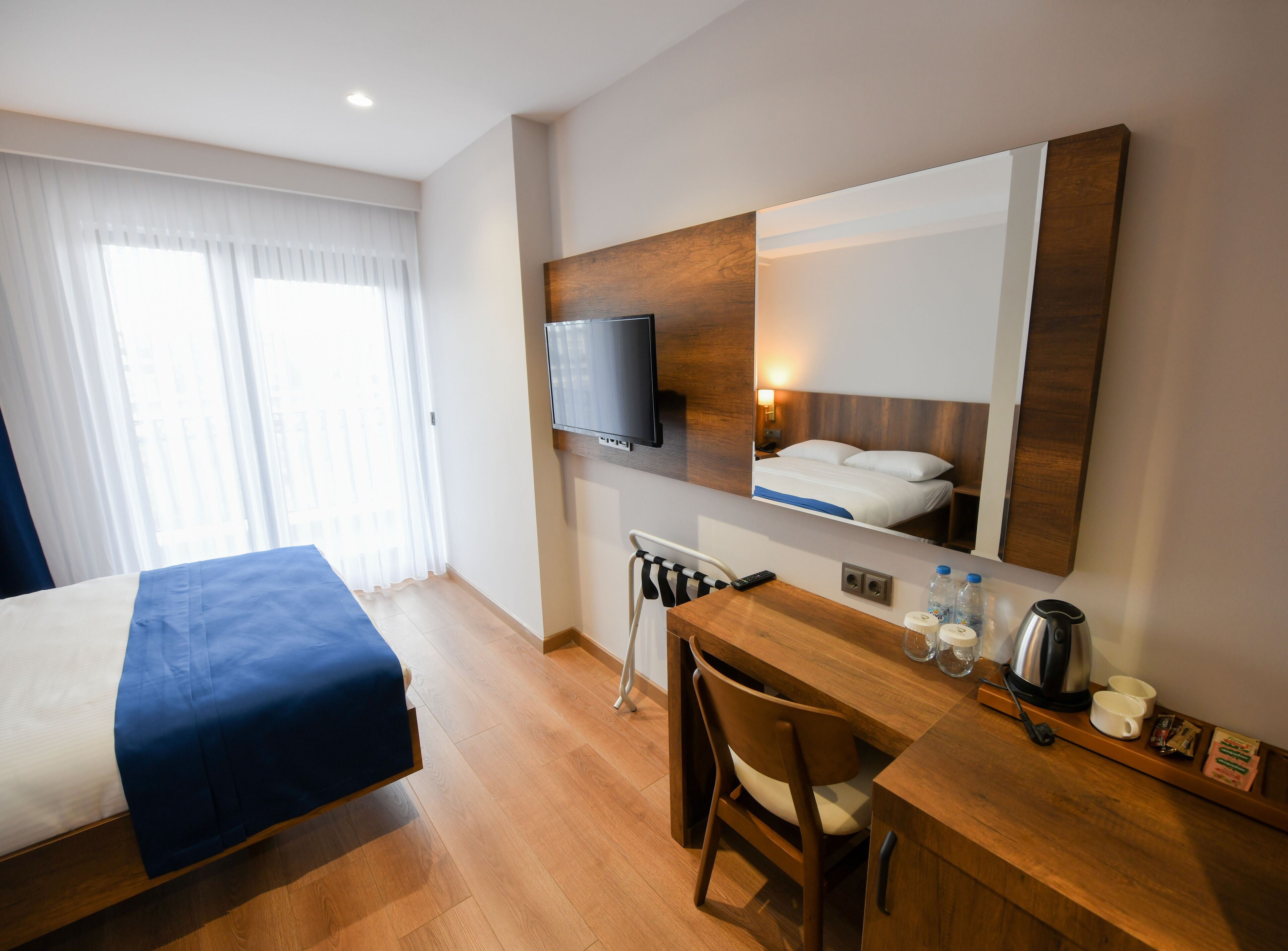 A hotel room with a bed, a desk with a chair, a television, and a mirror.