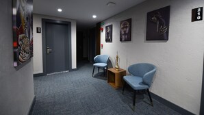 A hallway with two blue chairs, a small wooden table with a decorative item, and a door marked with the number 210. - Ref Inn Hotel (Ordu)