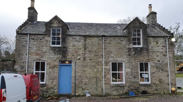 A stone building with a blue door, two windows, and a chimney.