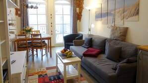 Una sala de estar acogedora con un sofá, una mesa de comedor con sillas y una pequeña mesa blanca con fruta.