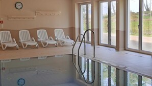 Zona de piscina con sillas reclinables blancas, un reloj y ventanas amplias.