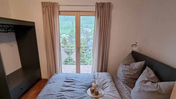 A bedroom with a bed, a dresser, and a window with curtains. - Spacious vacation apartment for 2 to 4 people surrounded by nature (Feldkirch)