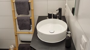 A bathroom with a round sink, a mirror, a towel rack, and a toilet. - Spacious vacation apartment for 2 to 4 people surrounded by nature (Feldkirch)