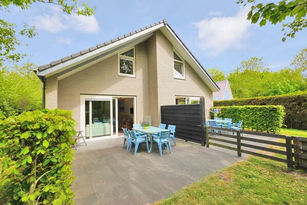 Ein zweistöckiges Haus mit Terrasse, einer Glastür und einem umzäunten Garten.