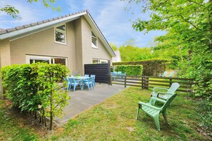 Ein Haus mit einer Terrassenanlage, komplett mit Tisch und Stühlen, umgeben von Grünpflanzen und einem Holzzaun.