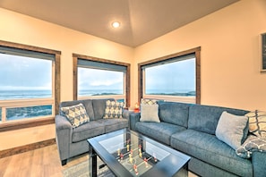 A living room with a sofa set, a glass coffee table, and large windows offering a view of the ocean.