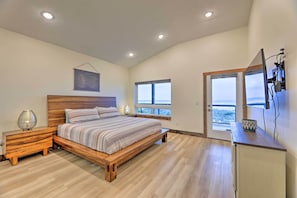 A bedroom with a wooden bed, a nightstand, a lamp, and a view of the ocean through a window.