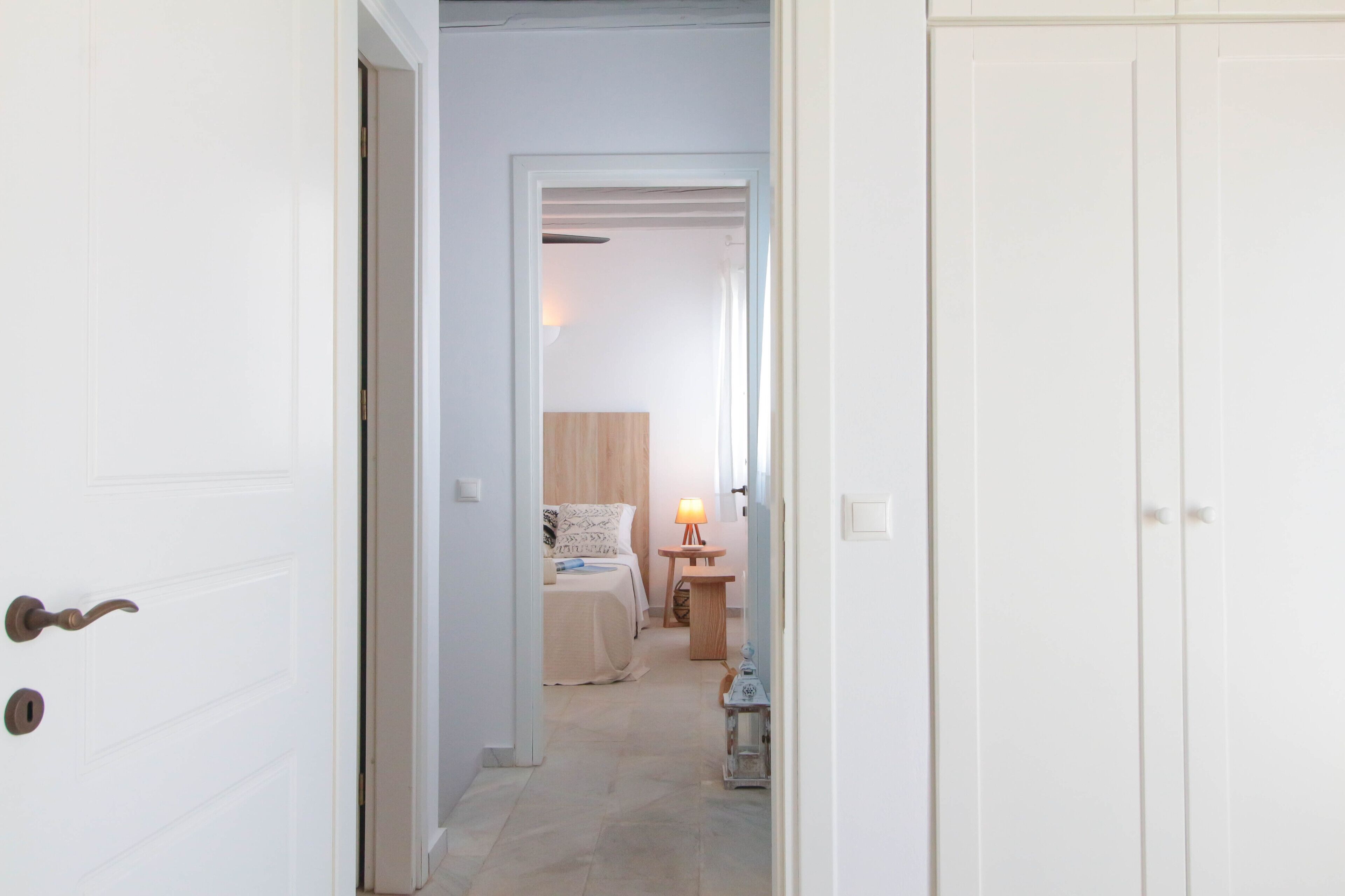 A hallway leading to a bedroom with a bed, bedside table, and lamp.