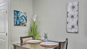 A dining table with two plates and a vase of flowers, flanked by chairs, in a room with a white door and a wall-mounted floral artwork. - 3 Mi to Downtown: Relaxing Stay in Edinburg Apt! (Edinburg)