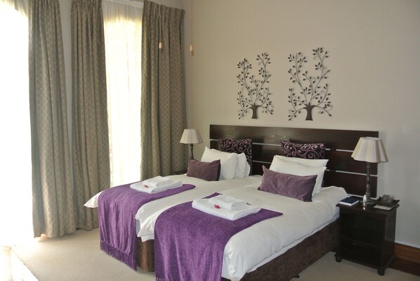 A hotel room with a large bed, two bedside tables, a nightstand, and a window with curtains. - Farmers Folly Guest House (Pretoria)