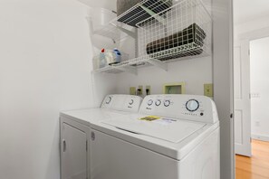A front-loading washing machine with control panels, a drying rack above it, and a door to the right.