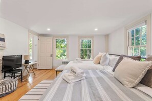 A bedroom with a bed, a desk with a computer, and two windows.