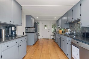 A modern kitchen with grey cabinets, stainless steel appliances, and a wooden floor.