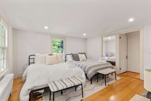 A bedroom with two beds, a bench, a radiator, and a window with curtains.