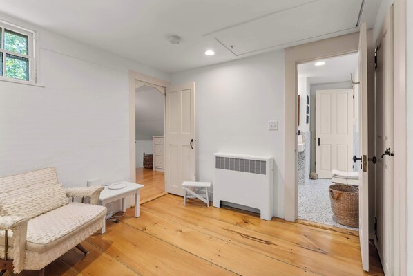 A room with a white sofa, a small table, a radiator, and a door leading to another room. - Mins to Beach, NEW AC and Game Room in 2026! (Barnstable)