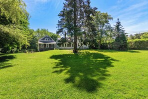 A residential property with a well-maintained lawn, a large tree, and a house with a gabled roof.