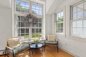 A room with large windows, wicker chairs, a round table, and a vase with flowers.