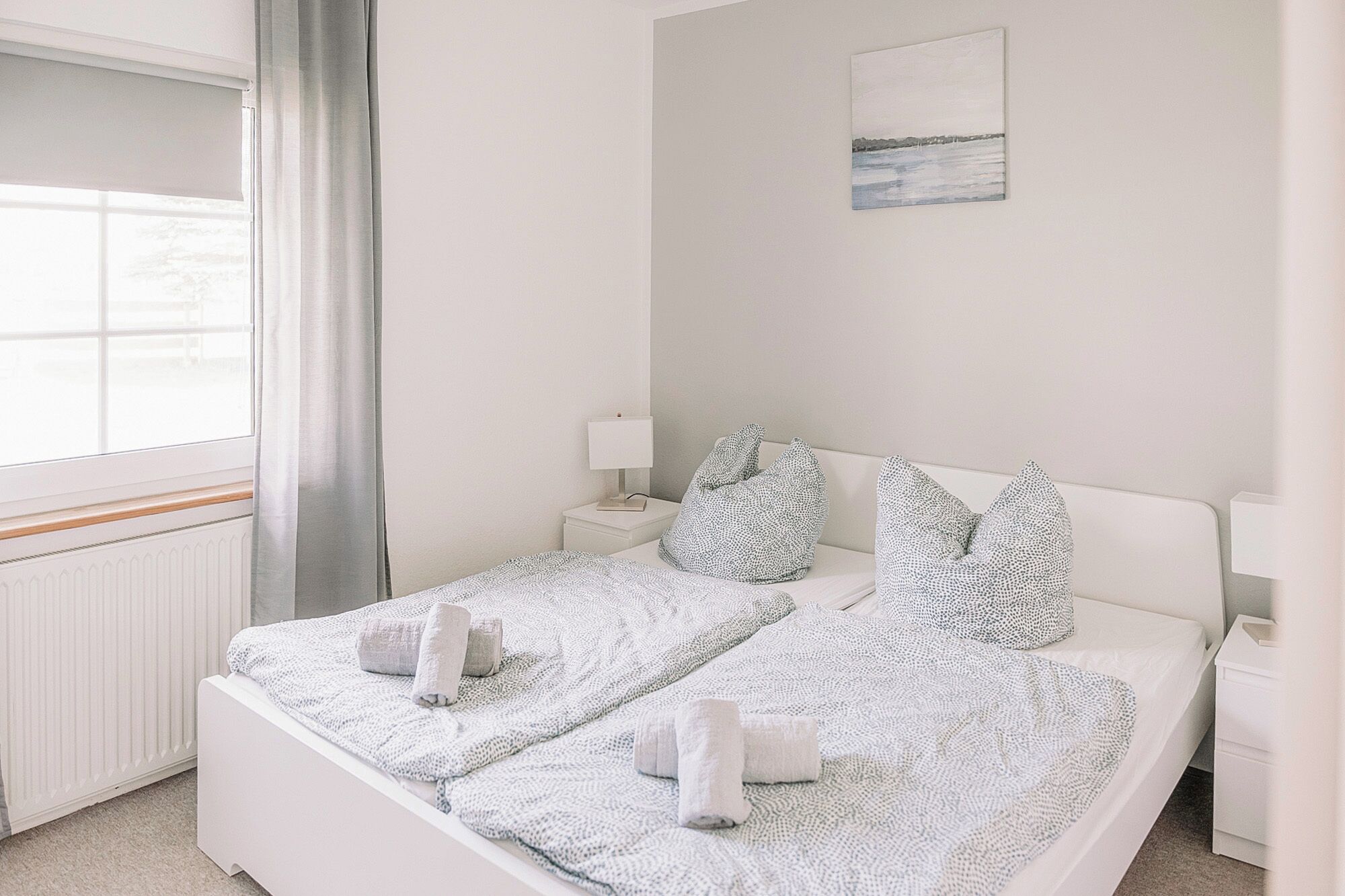Una cama bien hecha con toallas enrolladas, una mesita de noche con una lámpara, y un cuadro en la pared.