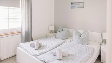 Una cama bien hecha con toallas enrolladas, una mesita de noche con una lámpara, y un cuadro en la pared.