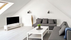 Ein modernes Loft-Wohnzimmer mit Flachbildfernseher, einem weißen Couchtisch, einem grauen Sofa und einer grauen Eckcouch.