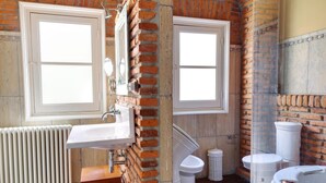 A bathroom with a white sink, two white toilets, a white bathtub, and a radiator.