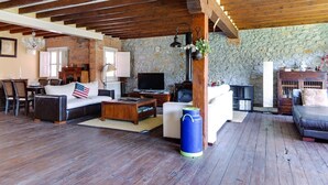 A spacious living room with a stone wall, wooden beams, a fireplace, and a television.