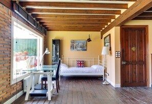 Une pièce comprenant un lit, un bureau, une chaise, une lampe, une fenêtre avec des stores, une porte et un tableau accroché au mur.