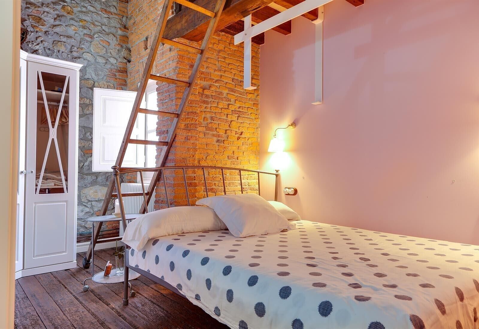 Un dormitorio con cama, escalera, armario y pared de piedra.