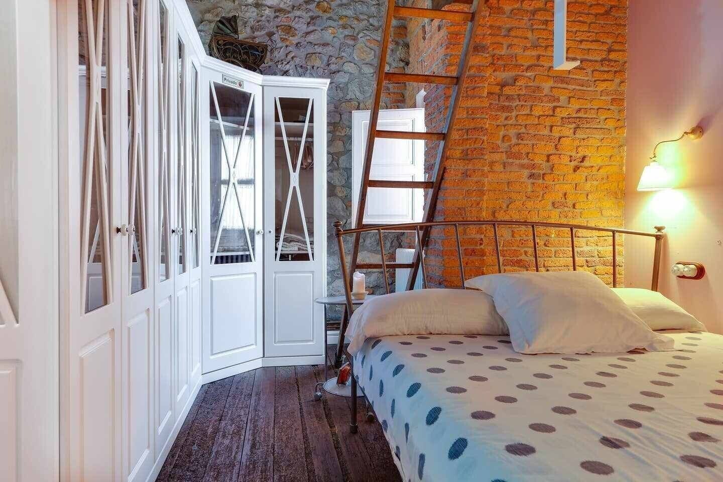 Un dormitorio con una cama, una escalera, un armario y un muro de ladrillo.