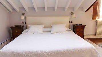 A bedroom with a large bed, two bedside tables, a headboard, and a window with a radiator.