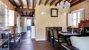A dining area with a wooden table and chairs, a chandelier, and a brick wall.