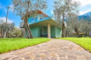 A modern building with a glass balcony, a stone pillar, and a paved pathway. - Holiday Home Casa Titi with Lake View, Garden, Private Terrace & Wi-Fi (Malcesine)