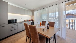 Eine moderne Küche mit grauen Schränken, einem Holztisch und Blick auf einen Berg durch große Fenster.
