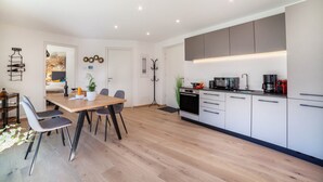 A modern kitchen with a dining area, featuring a wooden table, grey chairs, and built-in appliances.