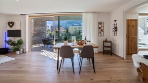 A modern living room with a dining area, large windows, and a view of buildings and mountains.