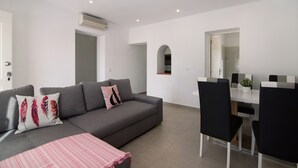 Een moderne woonkamer met een grijze bank, zwarte stoelen en een witte eettafel.