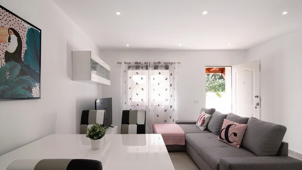 Een moderne woonkamer met een witte eettafel, een grijze bank en een televisie.