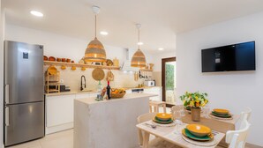 A modern kitchen with a central island, stainless steel refrigerator, hanging wicker pendant lights, and a flat-screen TV mounted on the wall. - Holiday Home "Ca Na Lola" Near the Beach with Wi-Fi, Air Conditioning & Terrace (Portocristo)