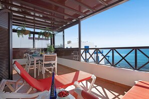 Un balcon avec une table et des chaises, une bouteille et un saladier de fruits.