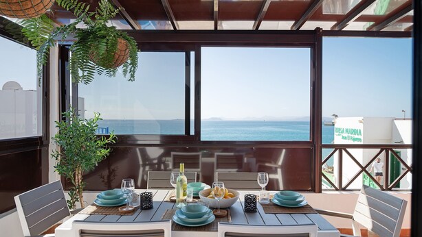 A dining area with a table set for four, overlooking the sea, with a view of the marina and buildings in the background. - Apartment "La Estrella" Near Beach with Panoramic Sea View, Terrace, A/C & Wi-Fi (Playa Blanca)