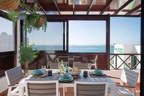 Un coin repas avec une table dressée pour quatre personnes, donnant sur la mer, avec vue sur le port de plaisance et les bâtiments en arrière-plan.