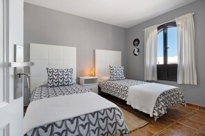 Une chambre avec deux lits, une table de chevet, une lampe, une fenêtre avec des rideaux et une horloge murale.